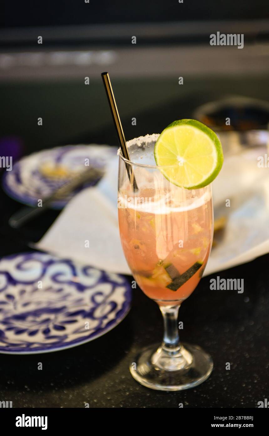 Ein gesalzter Rand auf Stemmware bietet einen Pink-Cocktail aus Gurken und Kalk mit Edelstahl-Strohhalm auf dem Bistrotisch im Freien Stockfoto