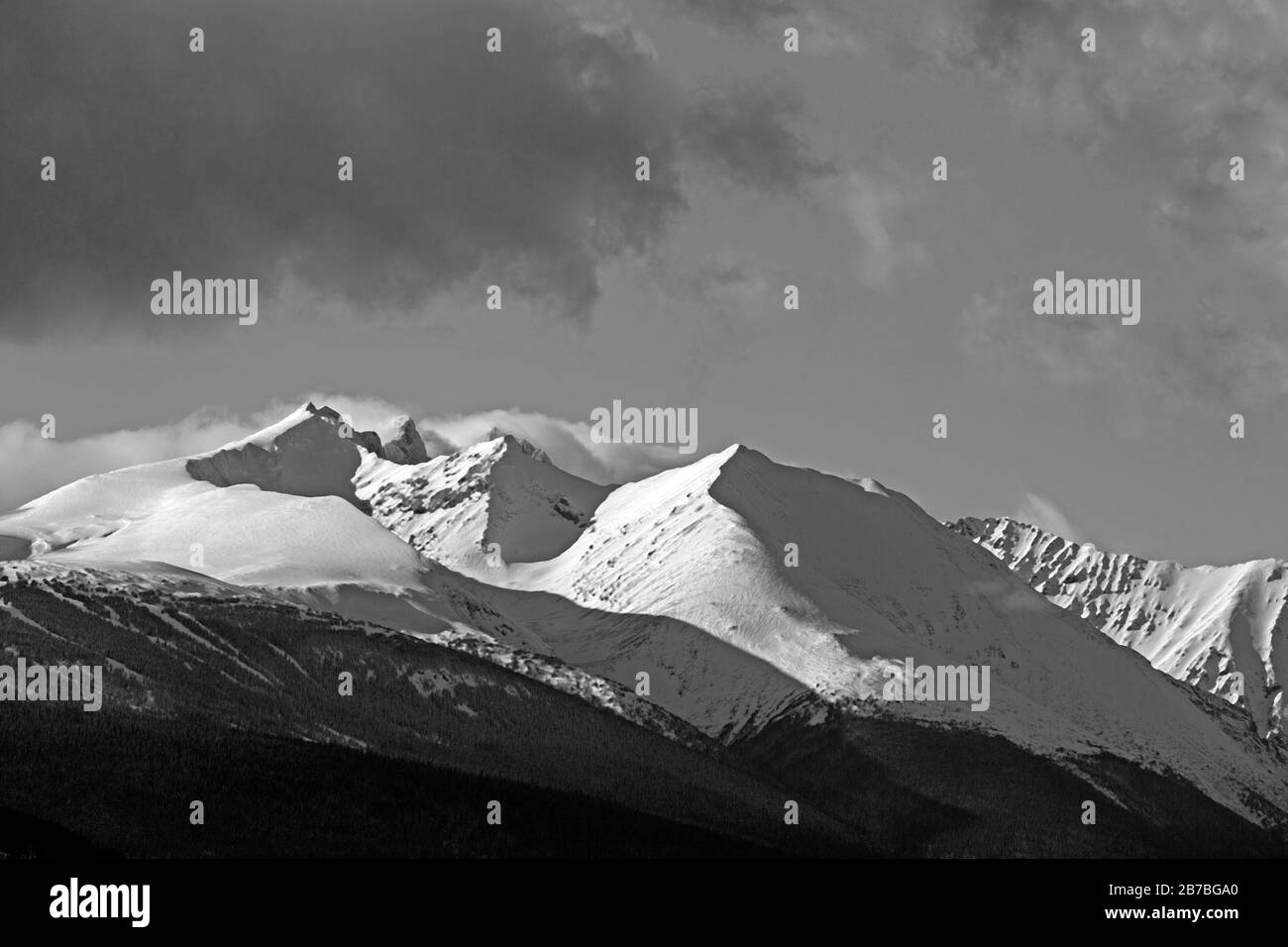 Winterlandschaft mit zerklüfteten Gipfeln und Sturmwolken über Mountain Range und Waldwildnis. Stockfoto