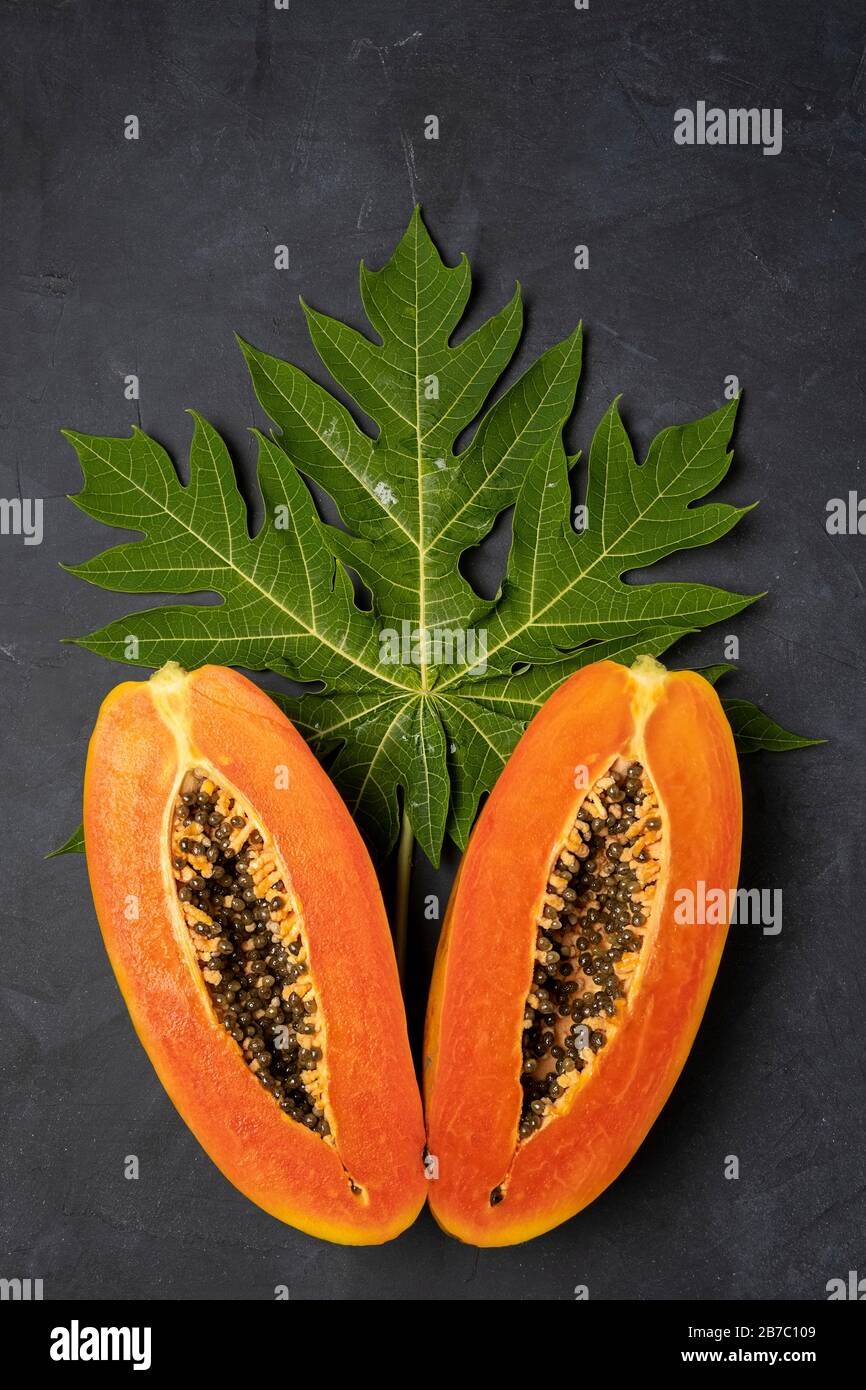 Zwei Hälften frisch geschnittener tropischer Papaya-Früchte, mit grünem Blatt auf dunklem Hintergrund, vertikaler Zusammensetzung Stockfoto