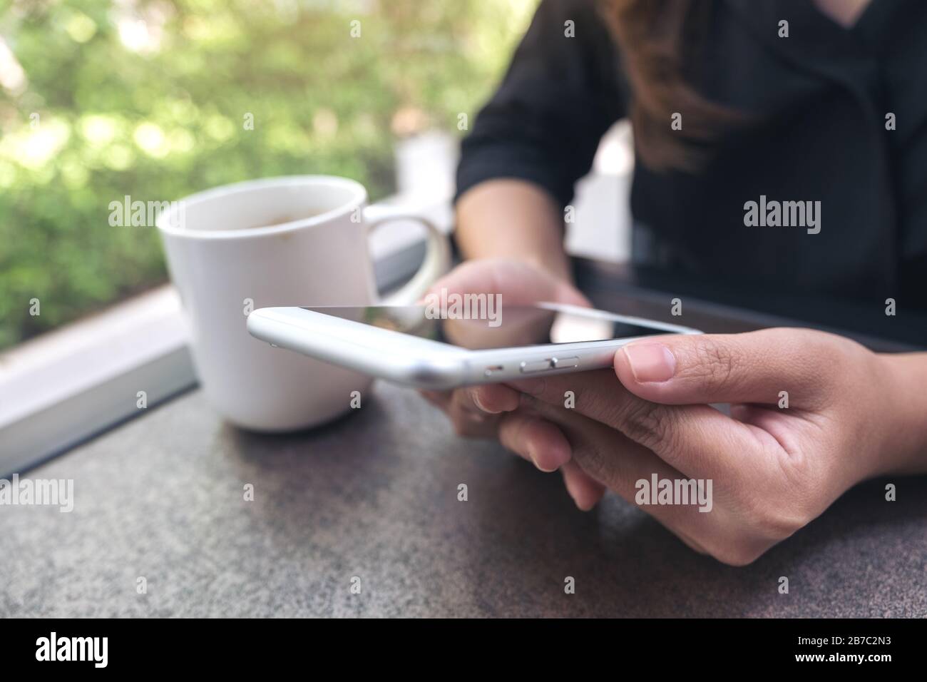 Nahaufnahme einer Frau, die ein Smartphone mit Kaffeetasse im Café verwendet und betrachtet Stockfoto