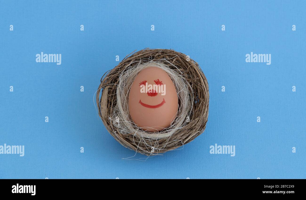 Fröhliches Osterei. Lustige Smiley-Gesichter auf einem Ei. Nisten Sie auf blauem Hintergrund. Osterei mit niedlichem, handgezeichnetes Gesicht. Stockfoto