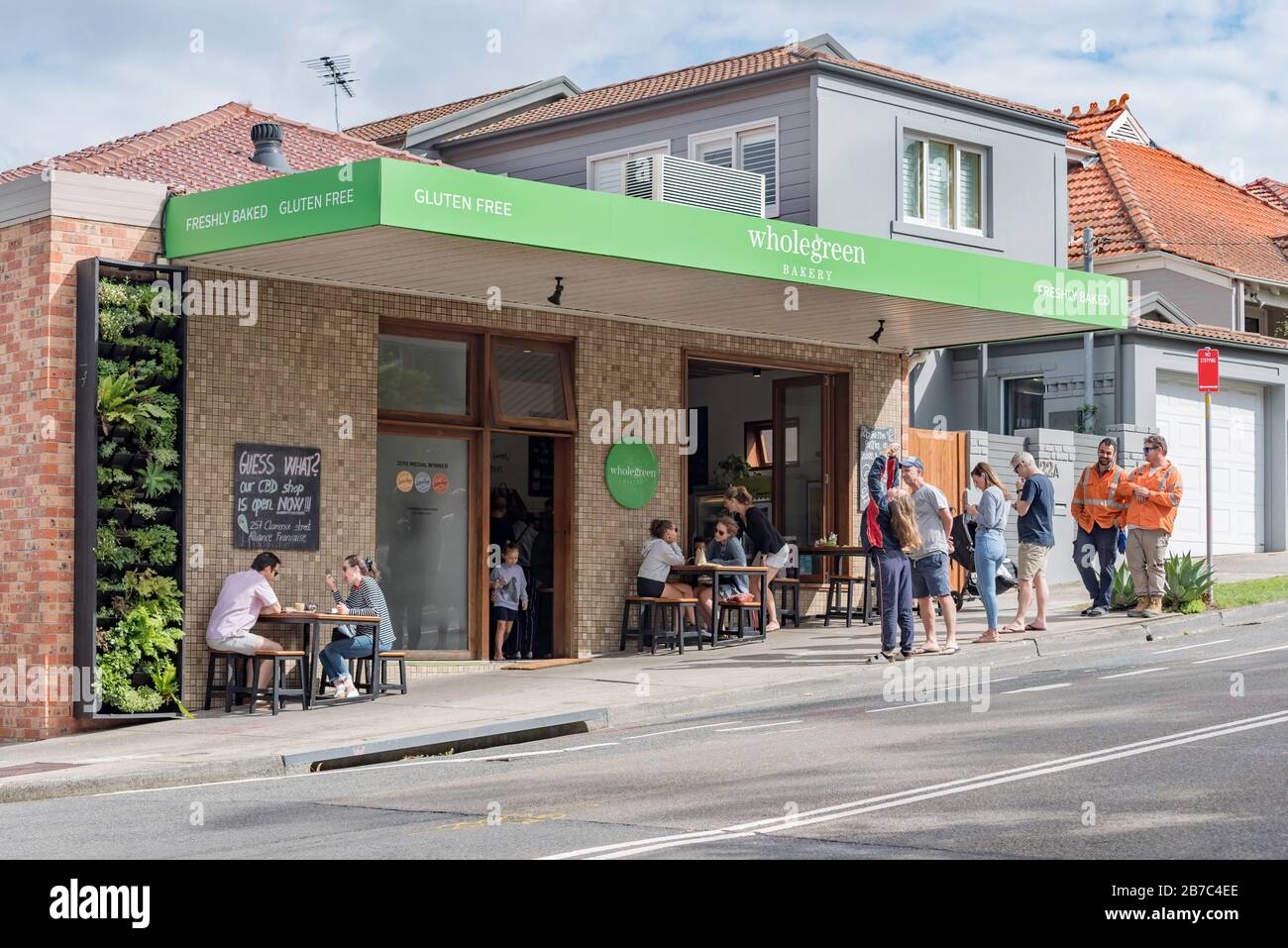 Die Leute warten und essen außerhalb der Wholegreen Bakery in Sydney, Australien, Vorort von Waverly. Wholegreen ist ein völlig glutenfreier Bäcker und Lieferant. Stockfoto