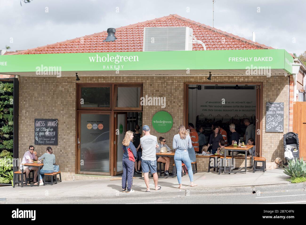 Die Leute warten und essen außerhalb der Wholegreen Bakery in Sydney, Australien, Vorort von Waverly. Wholegreen ist ein völlig glutenfreier Bäcker und Lieferant. Stockfoto