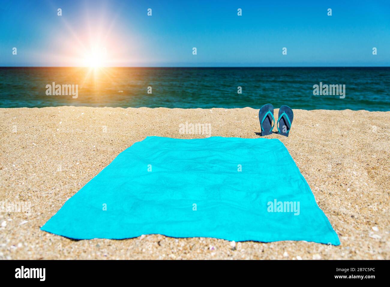 Blauer Sandalen-Flip-Flop und Handtuch auf gelbem Sand. Sommerspaß und Zubehör am Strand, Sommerferien, Kopieraum. Stockfoto