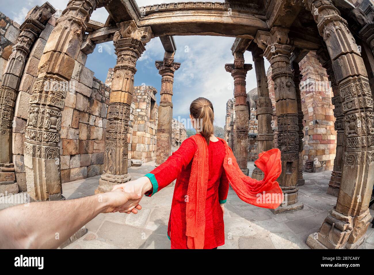 Frau in rotem Kostüm mit Schal, der Mann von Hand zum Qutub Minar Turm in Delhi, Indien führt Stockfoto