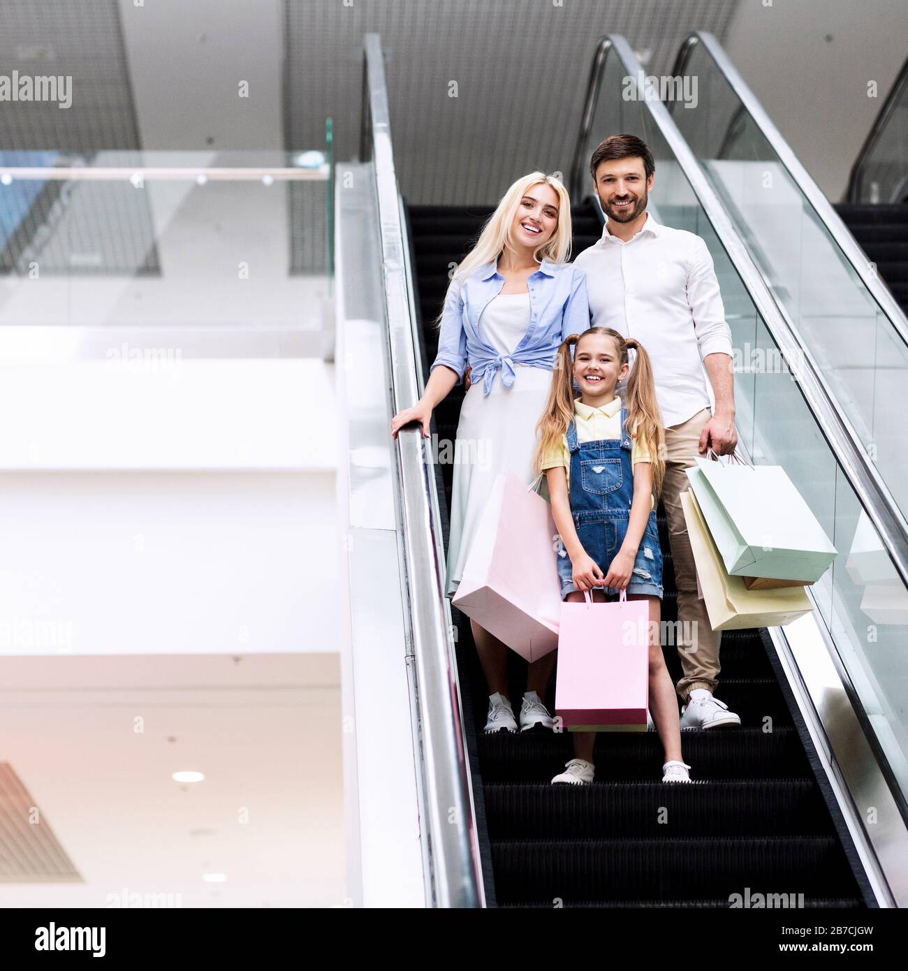 Eltern Und Tochter Holding Bags Stehen Auf Dem Escalator In Mall Stockfoto