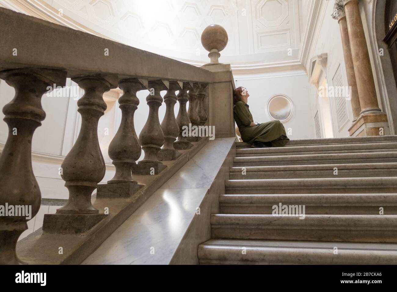 Eine Frau, die sich oben auf der großen Treppe im Archäologischen Nationalmuseum in Neapel, Italien, ausruht. Stockfoto