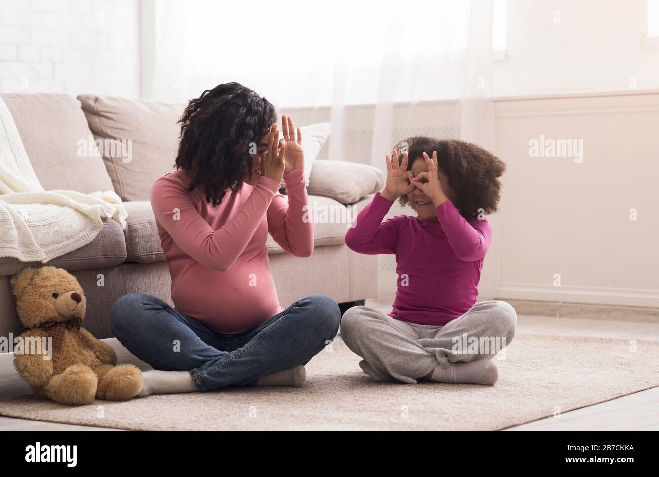 Verspielte Schwangere Mama Und Ihre Liebenswürdige Kleine Schwarze Tochter, Die Zu Hause Zusammen Tören Stockfoto