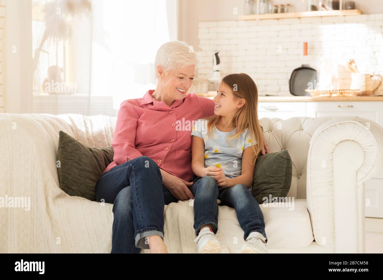 Fröhliche Granny mit ihrer Enkelin, die zusammen auf einem bequemen Sofa im Haus ruht Stockfoto