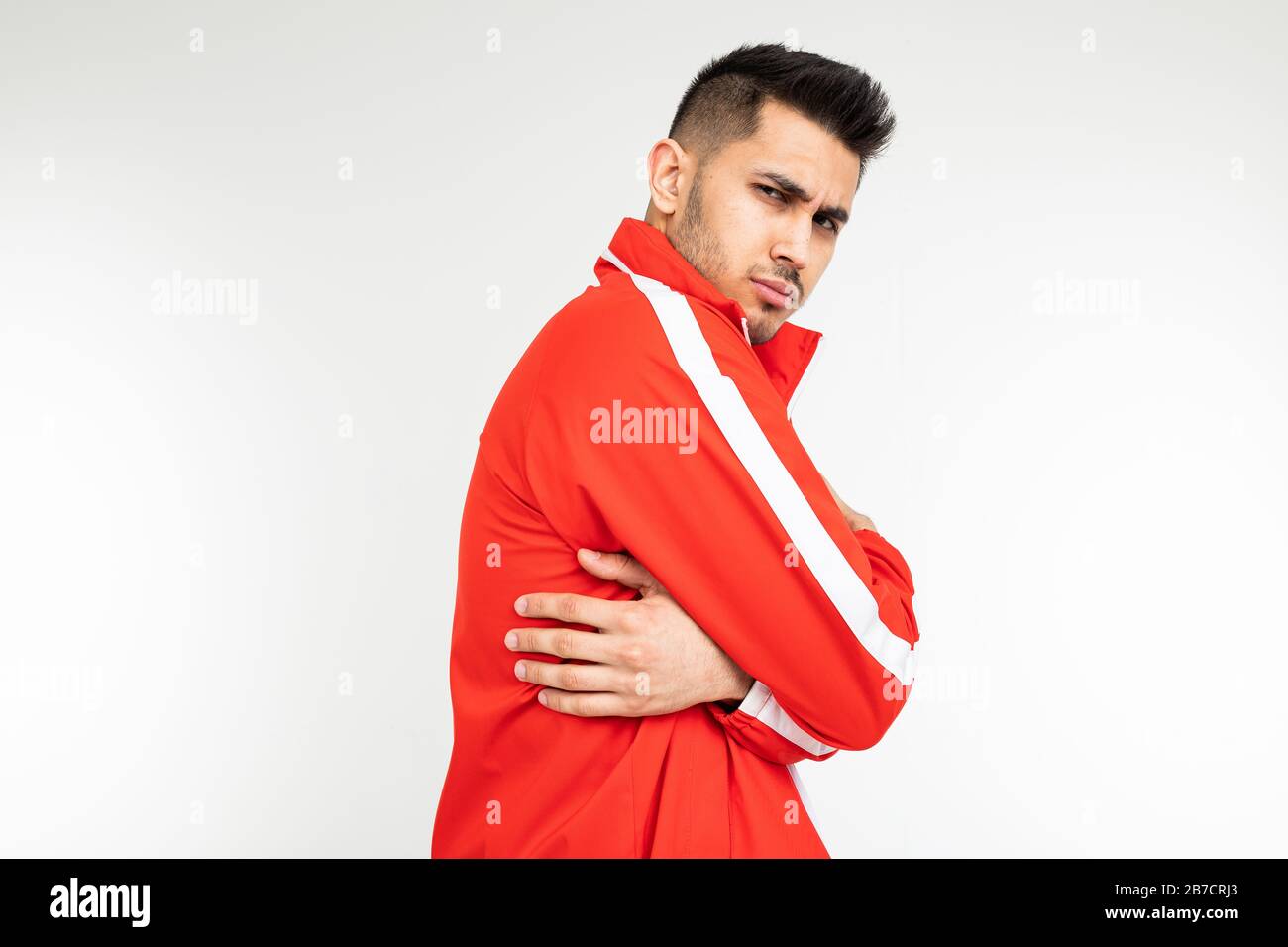 Der Mann in einem roten Sportanzug schrumpft vor der Kälte, die sich auf  einem weißen Hintergrund mit Kopierraum umarmt Stockfotografie - Alamy