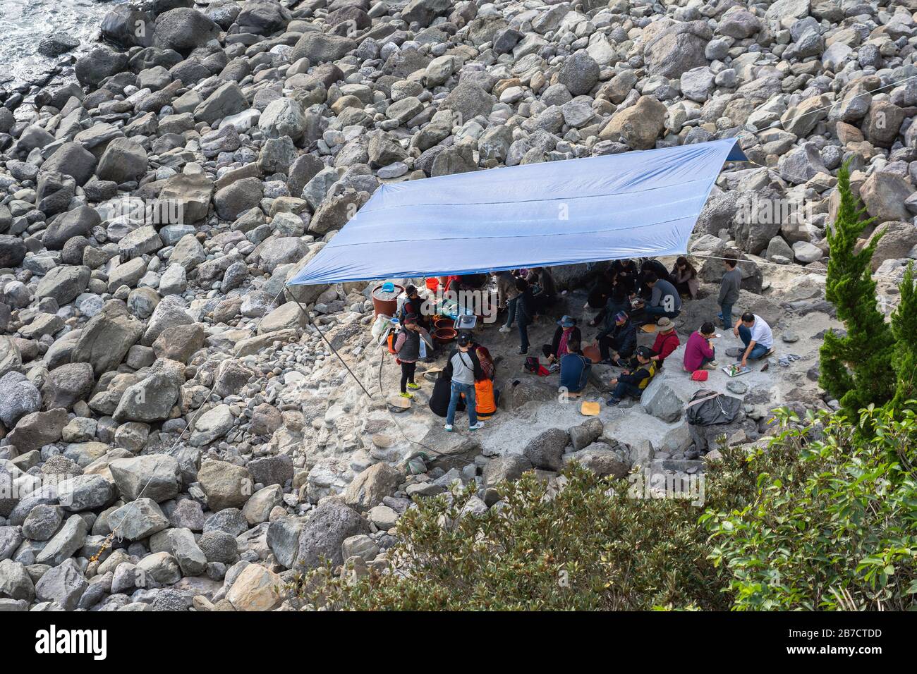 Gruppe asiatischer Menschen, die sich auf Stony Beach unter dem Zelt ausruhen und unterhalten. Koreanische Erwachsene kommunizieren unter Schutzraum.Chinese Tourist Spaß am Nat haben Stockfoto