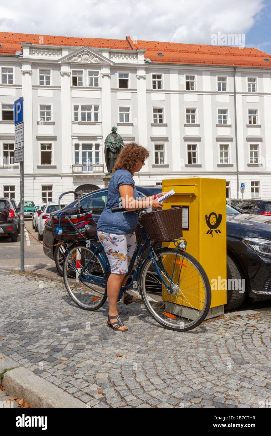 Frau auf dem Fahrrad Umschläge in eine Postbox der Deutschen Post in Regensburg, Bayern, Deutschland. Stockfoto