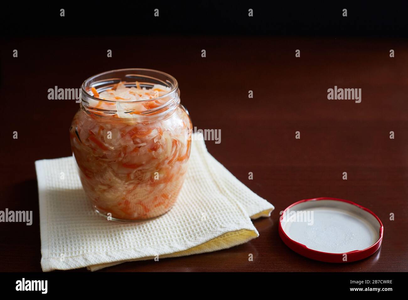 Glasbecher mit hausgemachtem Sauerkraut auf dunklem Hintergrund mit Copyspace. Aus Kohl und Karotten Stockfoto