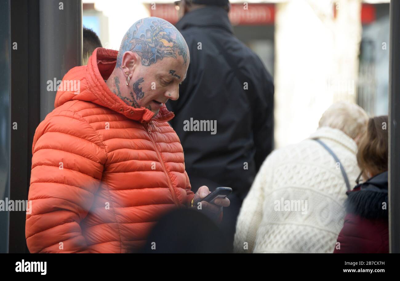 Tätowierte Mann in orangefarbener Jacke, die sein Handy überprüft. Stockfoto