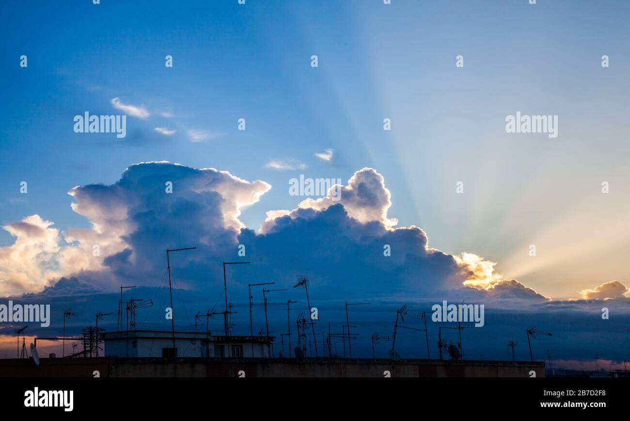 Sonnenstrahlen zwischen den Wolken über den Antennen auf den Dächern der Stadt Stockfoto