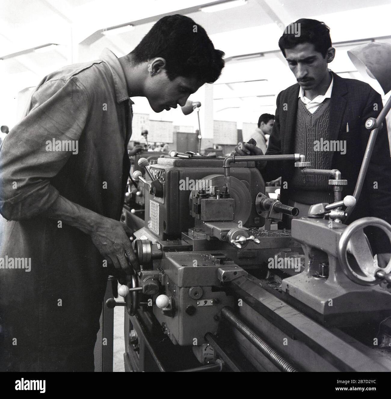 1960er Jahre, historisch, ein männlicher Ingenieurlehrling, der mit einer Werkzeugmaschine arbeitet, der von einem Manager, Saudi-Arabien, beaufsichtigt wird. Stockfoto