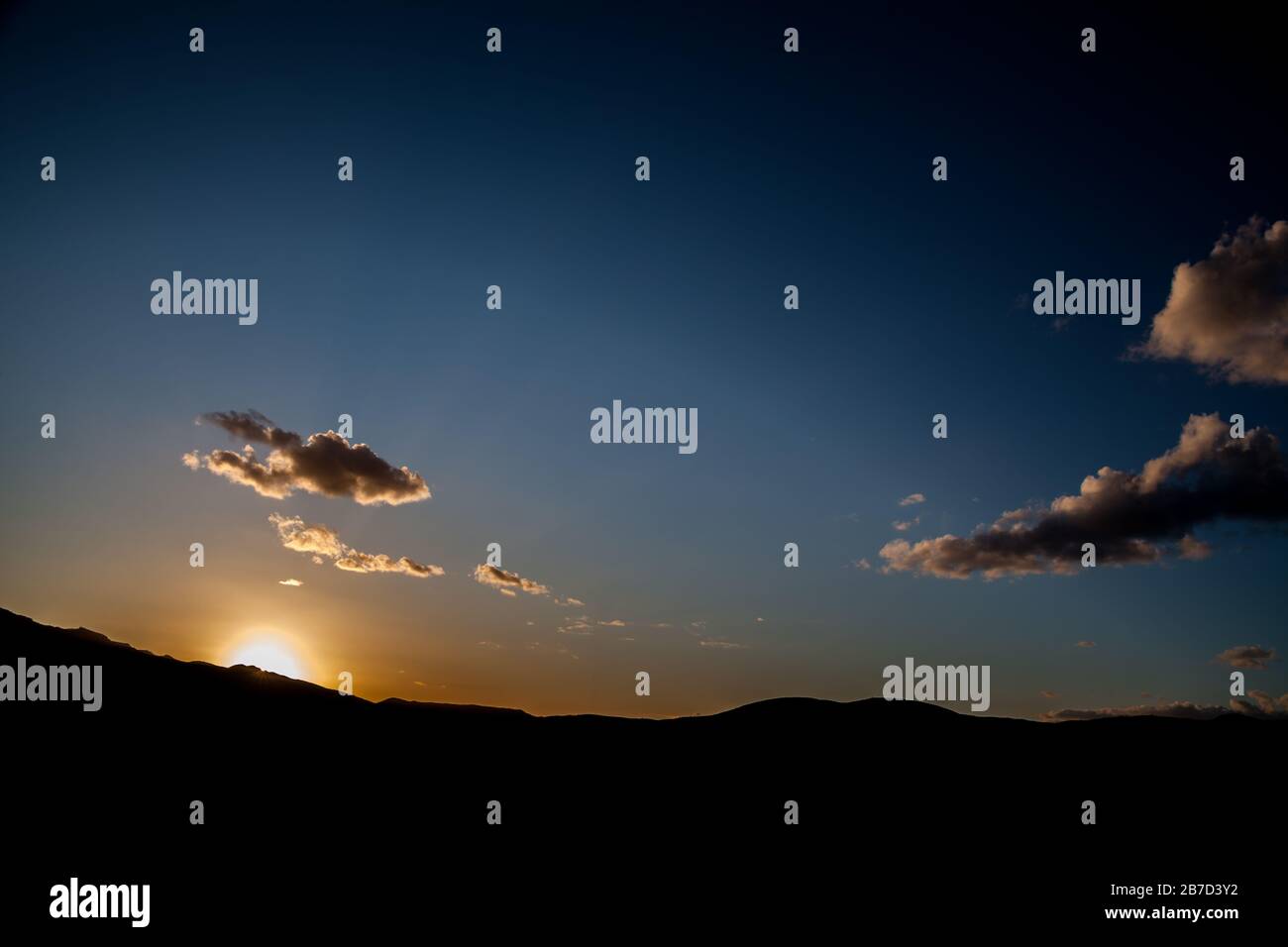 Sonnenuntergang hinter den Bergen mit Wolken, blauem Himmel und Sonnenstrahlen Stockfoto