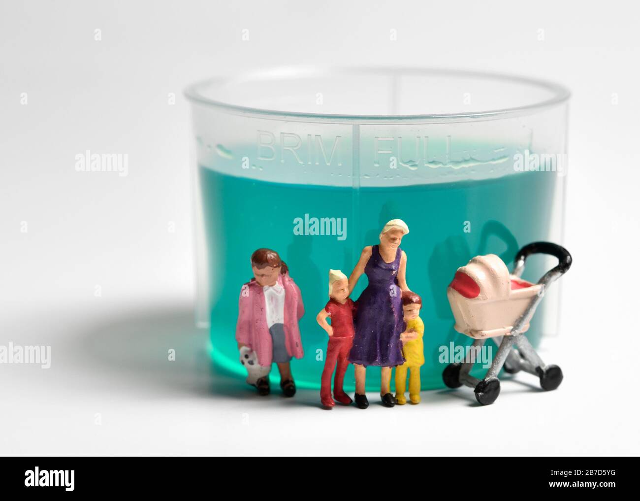 Miniatur-Figurin-Alleinerziehende, die vor einem Plastikbecher für flüssige Medikamente vor weißem Hintergrund steht. Stockfoto