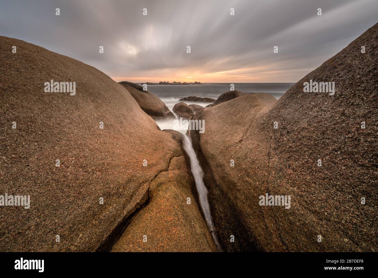 Eine schöne, nebelige Langzeitbelichtung, die bei Sonnenuntergang aufgenommen wurde, mit sich bewegenden Wolken im dramatischen Himmel und großen Felsen im Vordergrund Stockfoto