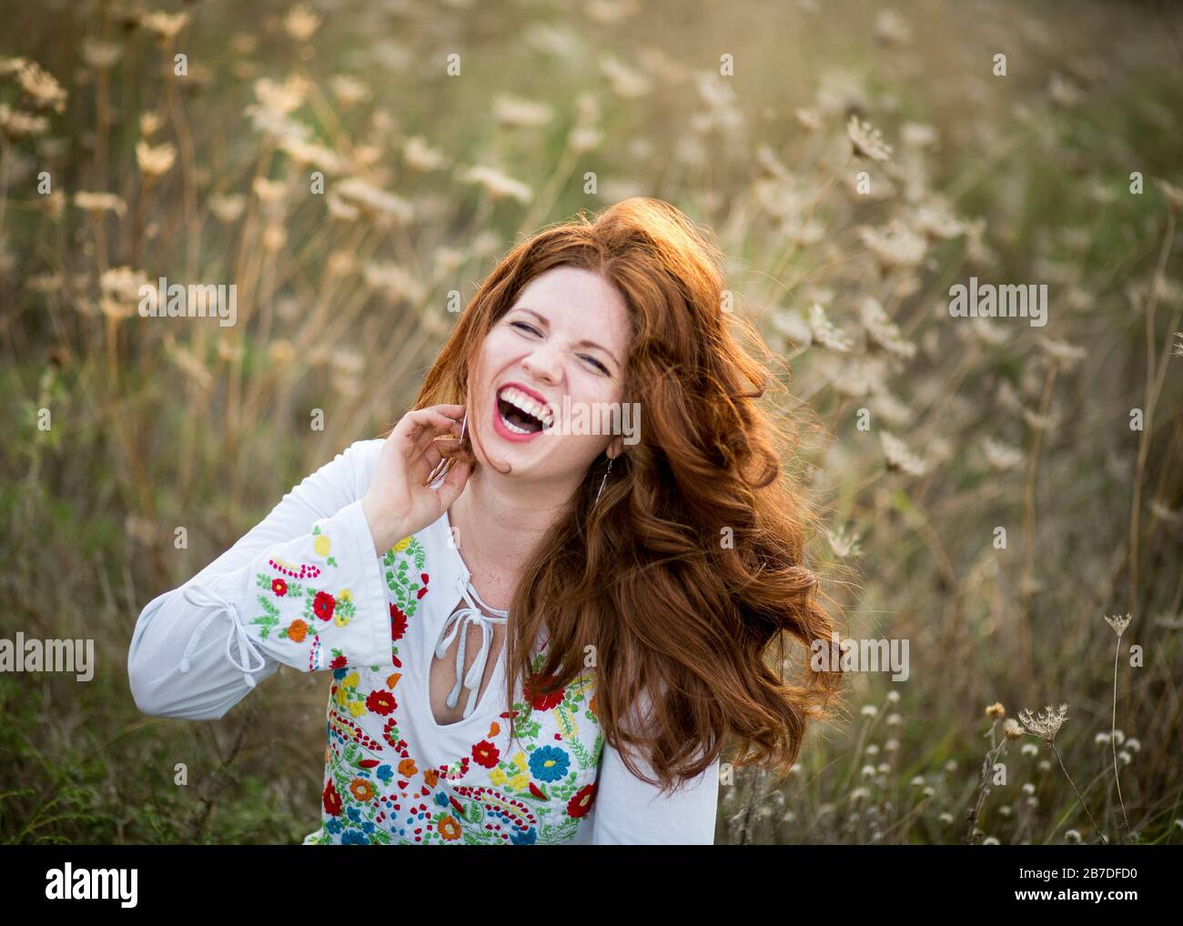 Fröhliche junge Frau mit prächtigen langen roten Haaren lacht tief und wirft Haare zurück Stockfoto