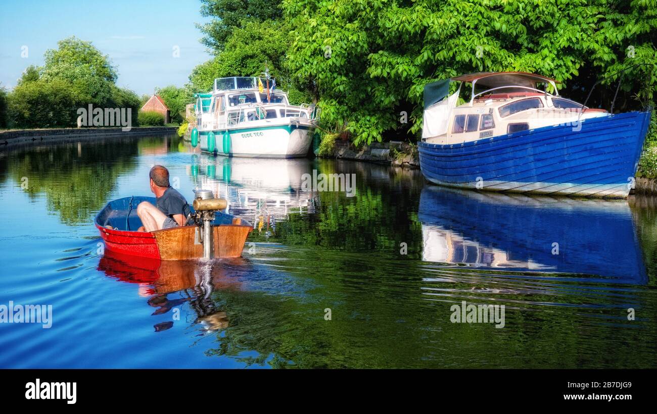 Schlauchboot mit Seagull Außenbordmotor, der entlang des Flusses Soar an vertäuten Booten vorbeifährt, in Leicestershire, England, Großbritannien, Großbritannien, Stockfoto