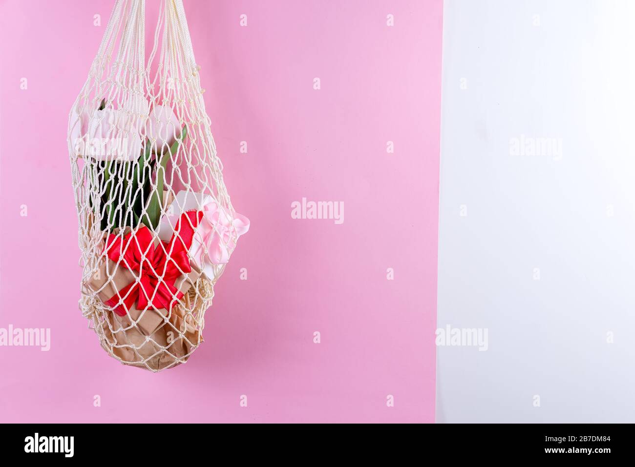 Wiederverwendbare Einkaufstaschen mit Geschenkschachteln aus Papier und frischen Tulpen im Frühling Blumen in der Hand der Frau vor einem rosafarbenen Hintergrund. Stockfoto