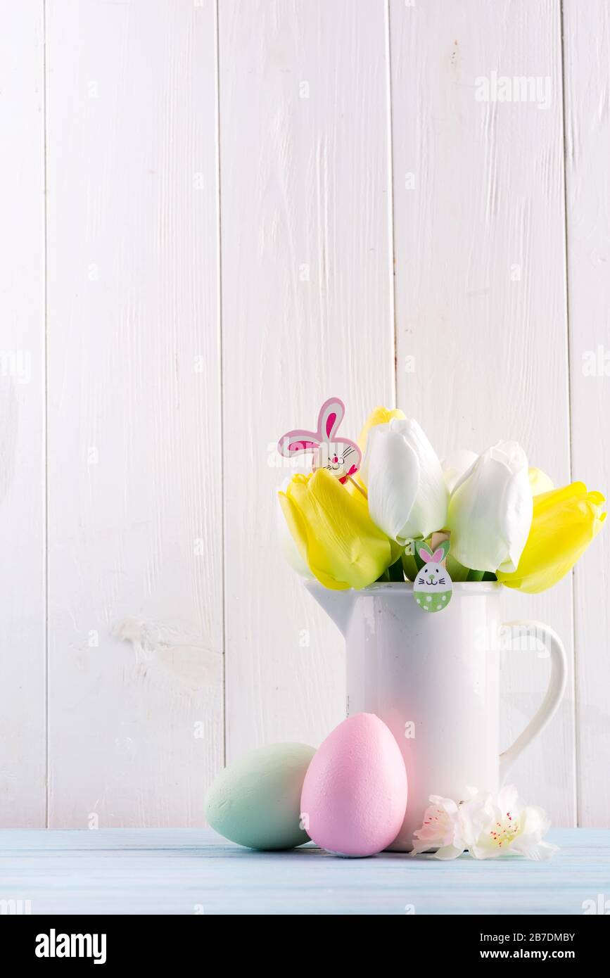 Glückwunschkarte für Ostern mit frischen Tulpen, handgemalten Eiern und Dekotation vor hellgrauem Holzhintergrund. Stockfoto