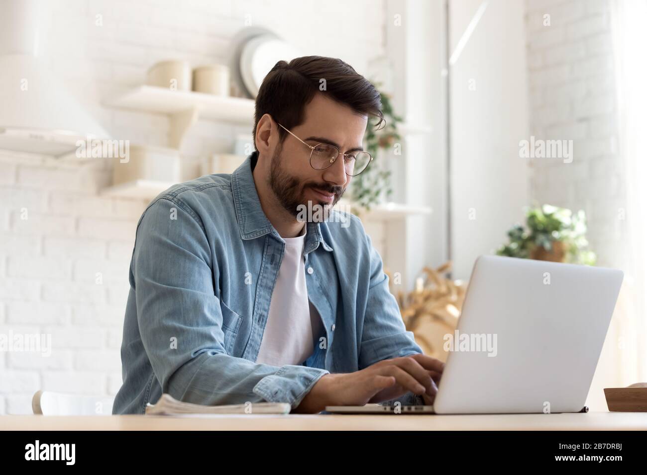 Konzentrierter junger Mann, der mit einem Laptop eine Brille trägt und auf der Tastatur tippt Stockfoto