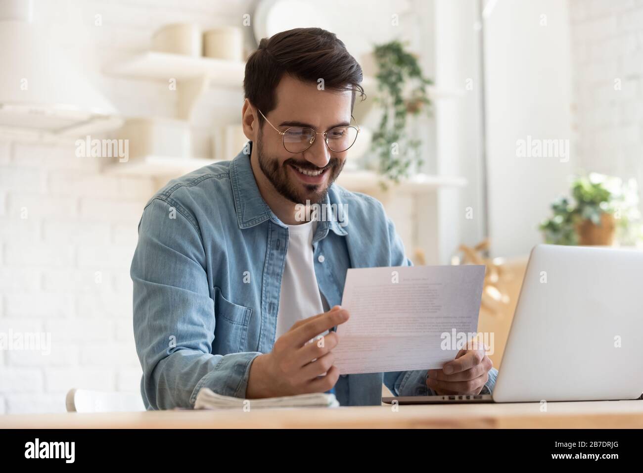 Lächelnder junger Mann liest gute Nachrichten in Papierbenachrichtigung Stockfoto
