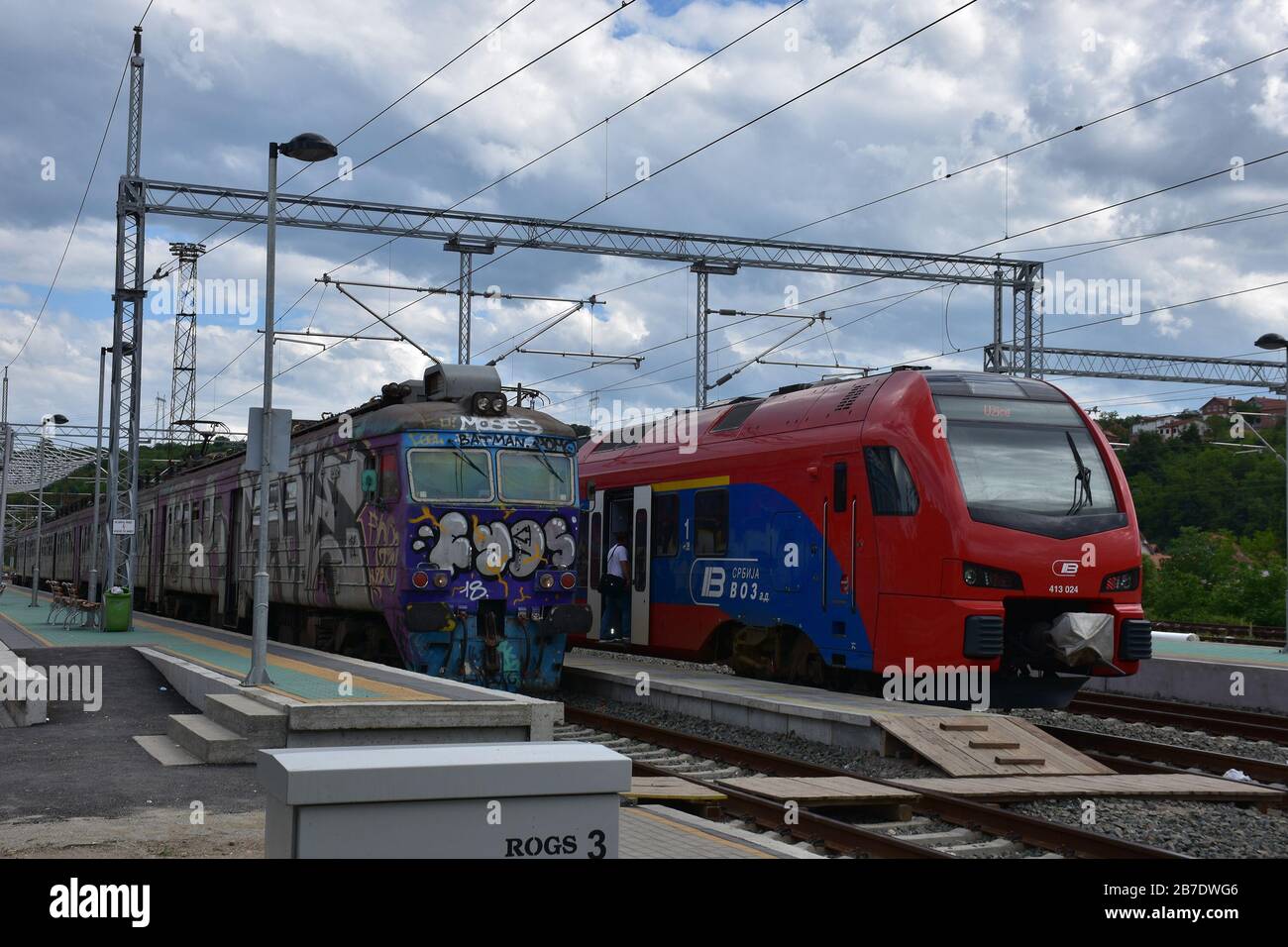 Am Bahnhof stehen zwei Züge nebeneinander. Das eine ist neu und rot ist blau und das andere ist bunt und alt Stockfoto