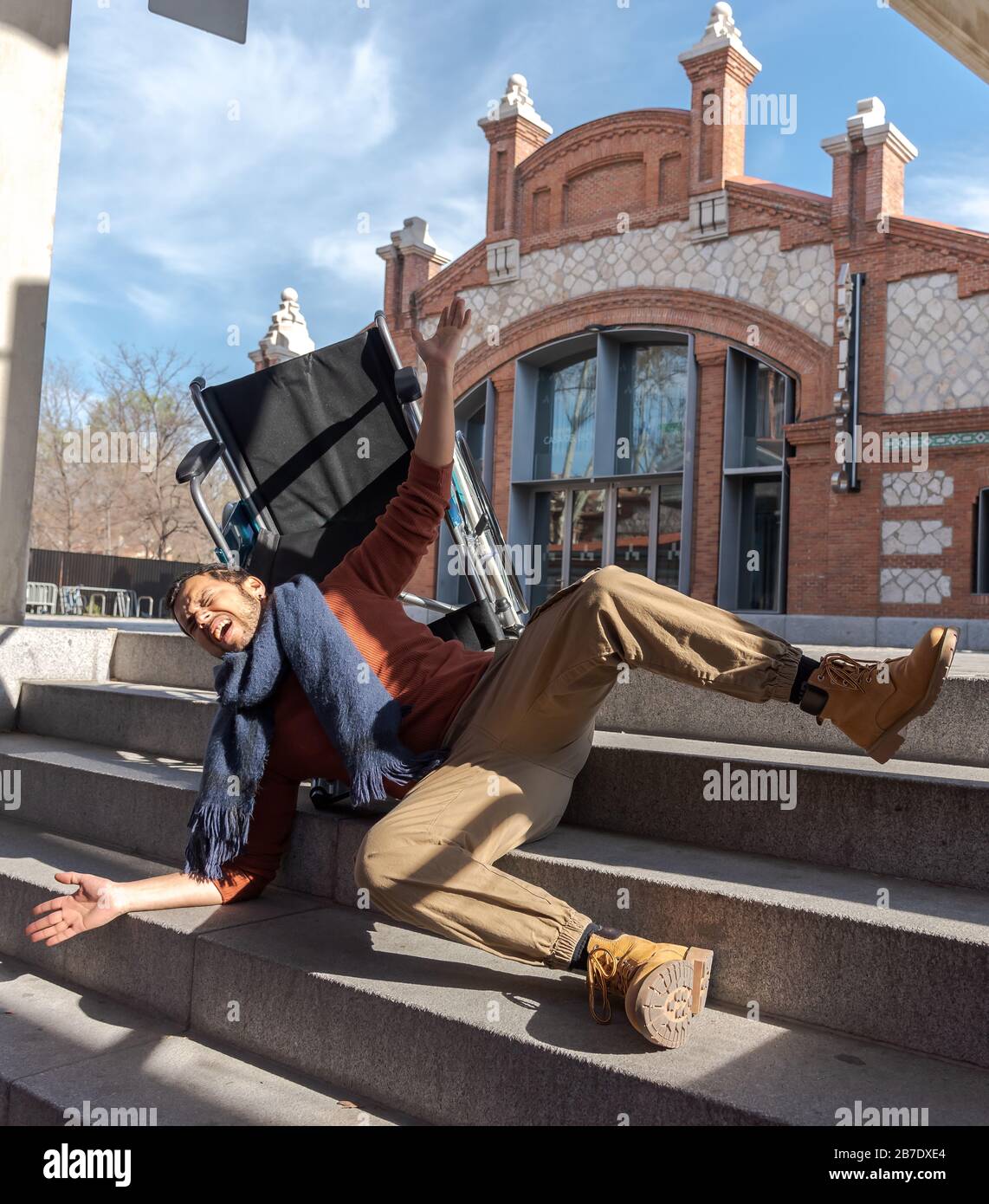 Behinderter Latino-junger Mann im Rollstuhl fällt eine Treppe hinunter, die er nicht mit dem Stuhl auf der Straße hinuntergehen kann Stockfoto