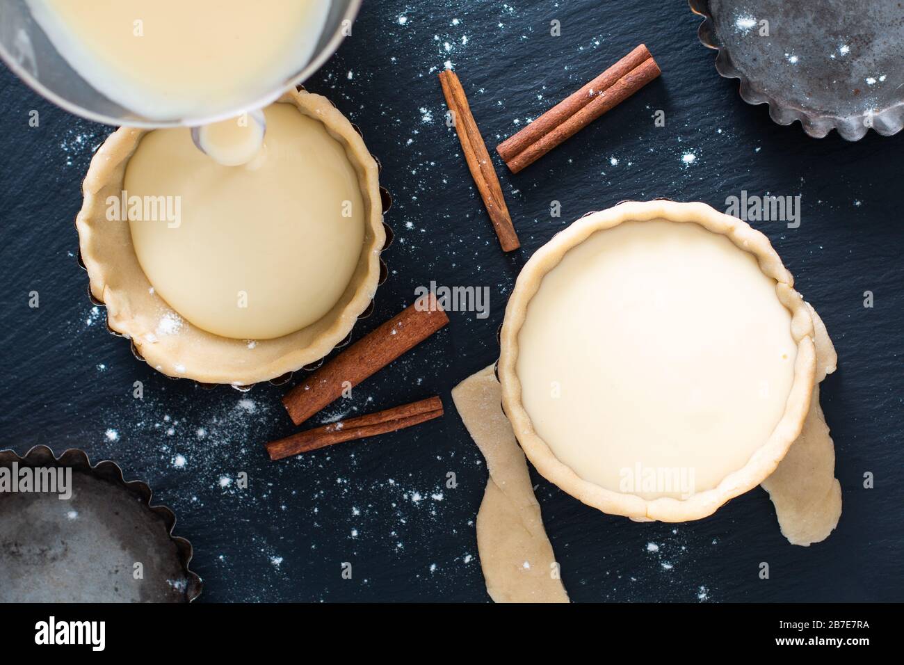Lebensmittelkonzept hausgemachtes organisches Ei Portuguese Custard tarts PASTEis DE NATA auf schwarzem Schiefersteinplatte Stockfoto