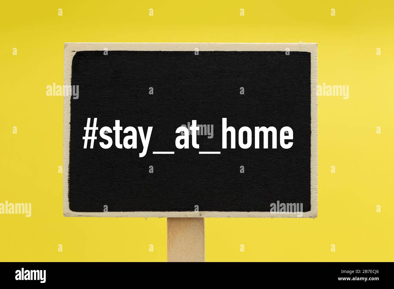 Bleiben Sie zu Hause mit Hashtag auf einem Schwarzen Brett vor gelbem Hintergrund - Gesundheitswesen Stockfoto