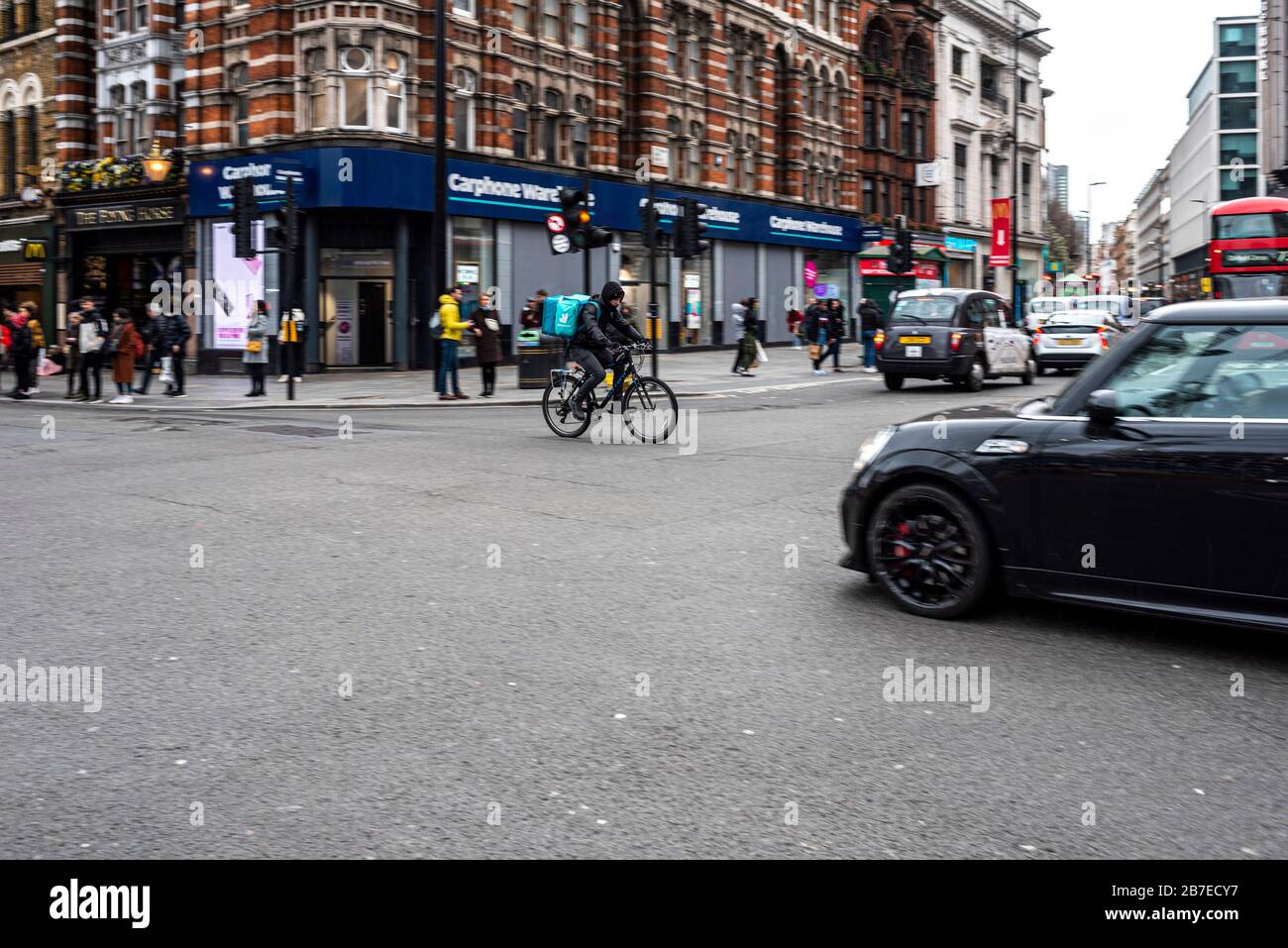 London, Großbritannien. März 2020. Deliveroo Radfahrer eilen durch die Tottenham Court Road Kreuzung. Während die großen Länder in der totalen Sperre sind, hat Großbritannien immer noch Stockfoto