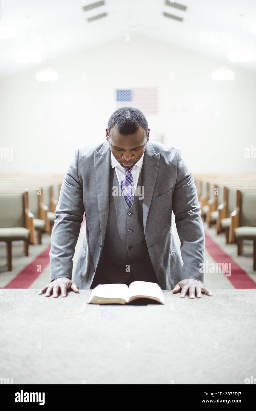 Afroamerikanischer Mann, der mit dem Kopf nach unten betet und auf die schaut Bibel in der Kirche Stockfoto