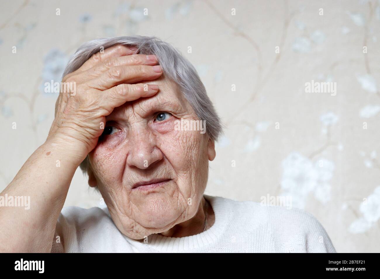 Coronavirus Symptome, ältere Frau legte ihre Hand auf die Stirn. Krankes Weibchen mit grauem Haar, Kopfschmerzen, Druck oder Kälte und Grippe Stockfoto