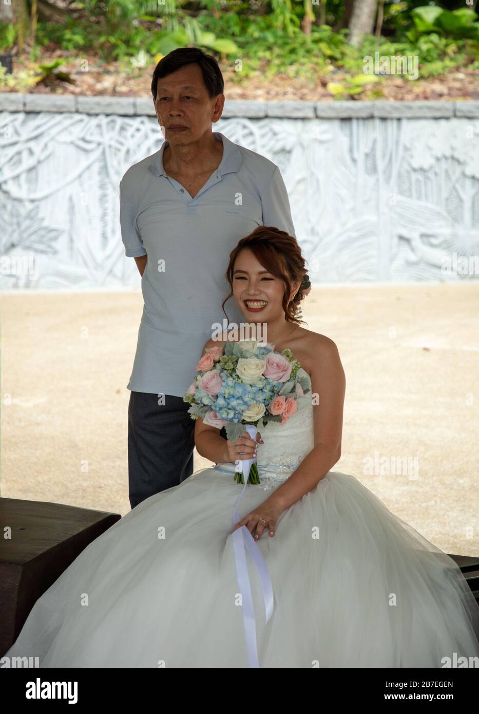 Brautpaar im Hochzeitskleid und mit Blumenstrauß in Botanischen Gärten in Singapur Stockfoto