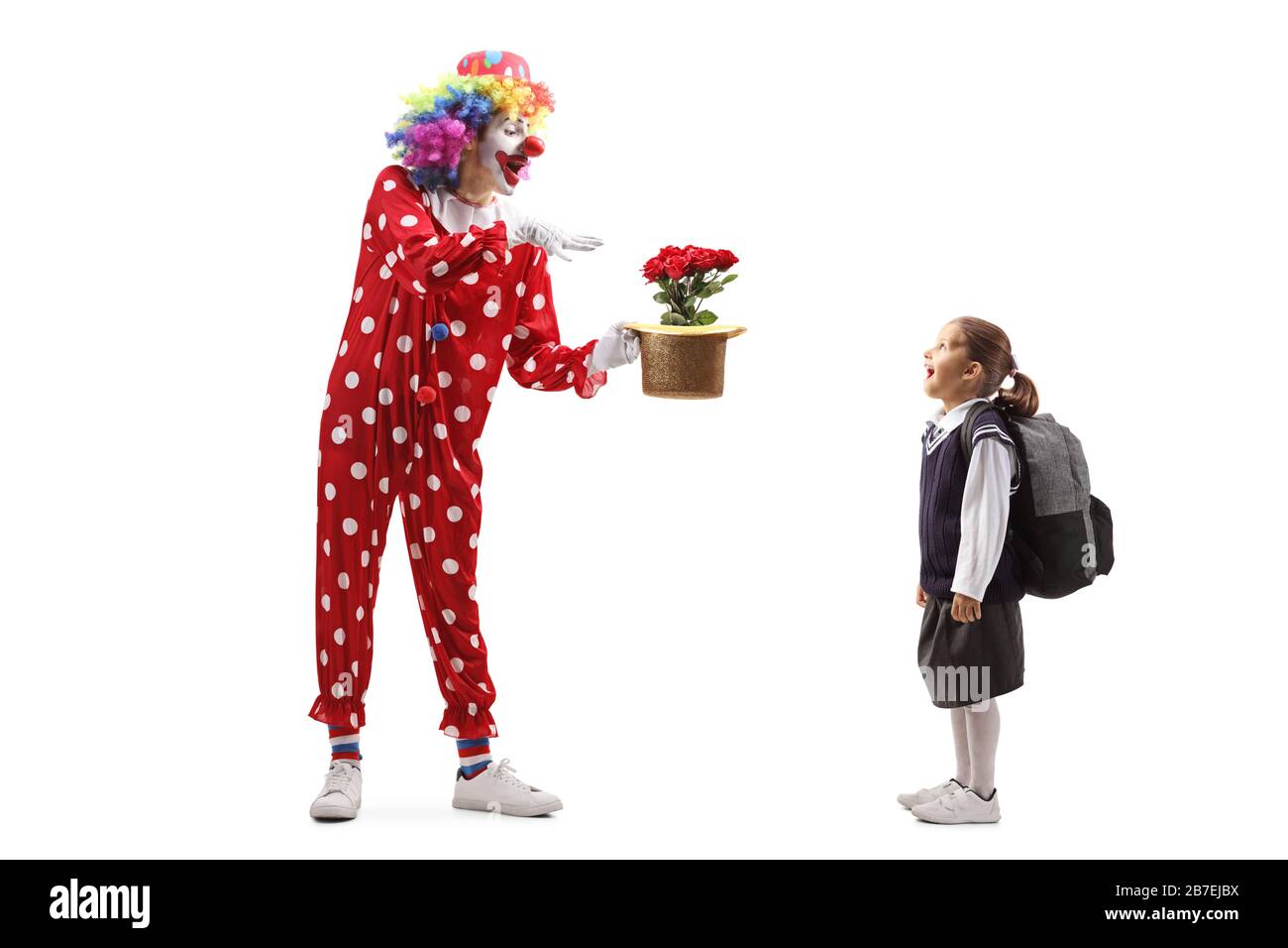 Lange Aufnahme eines Clowns, der einen Trick mit Blumen und Hut ausführt, und eines Schulmädchens, das isoliert auf weißem Hintergrund beobachtet Stockfoto