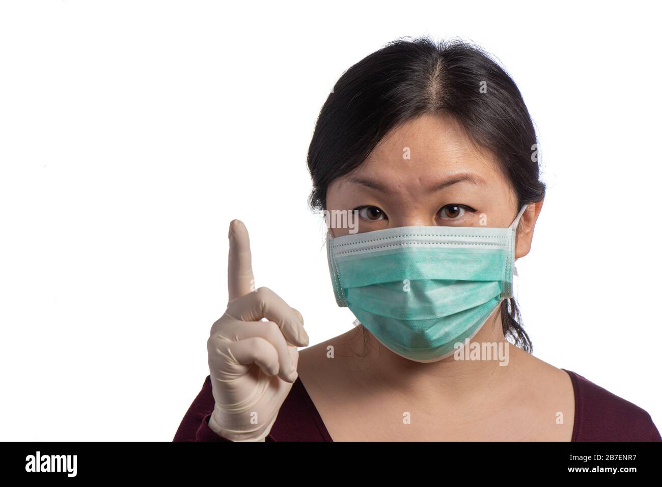 Junge asiatische Frau, die eine grüne Schutzmaske mit medizinischen Handschuhen trägt, macht auf weißem Hintergrund Vorsicht Stockfoto