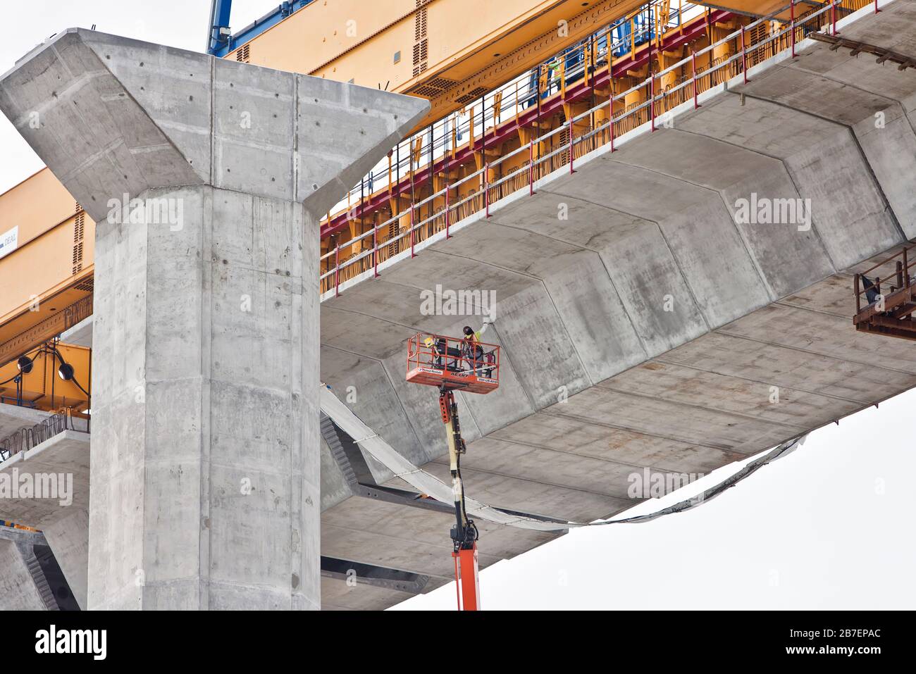 Neue Hafenbrückenkonstruktion, Arbeiter mit verlängertem Kraftheber ausgesetzt, die Zementverbindungen unter der Brücke reinigen. Stockfoto