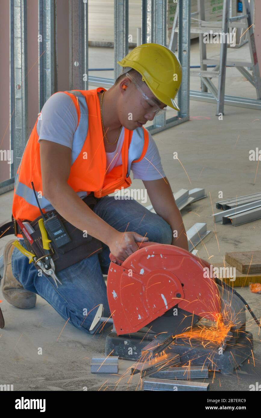 Handwerker schneiden mit einer Metallsäge an der Arbeit an einem neuen Architekturprojekt und tragen Hemd, Stiefel, Helm, Brille und Kniepolster mit hoher Sichtbarkeit. Stockfoto