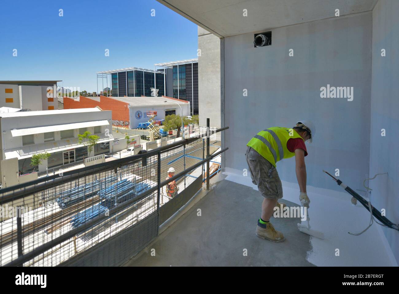 Handwerker bei der Arbeit auf dem Balkon eines neuen Architekturprojekts, das Hemd, Stiefel und Kniepolster mit hoher Sicht trägt. Stockfoto