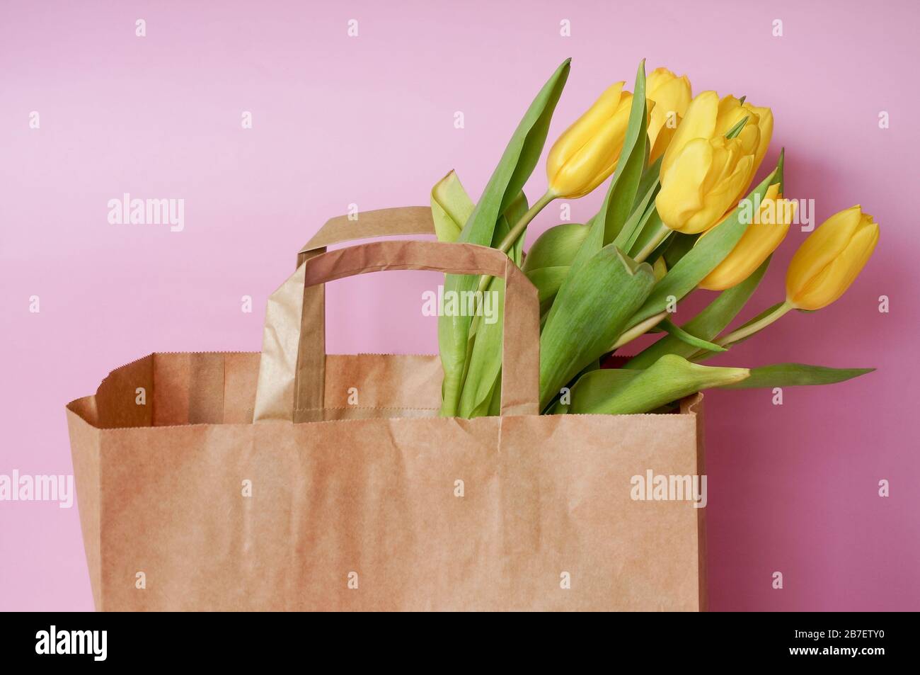 Gelber Tulpen-Blumenstrauß in brauner Papiertüte auf rosenfarbenem Hintergrund Stockfoto