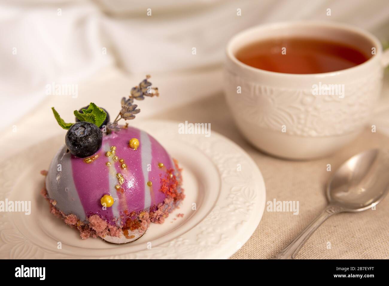 Stillleben mit einer Tasse Tee und süßem Kuchen auf weißem Holztisch. Frühstück in der Morgensonne Stockfoto