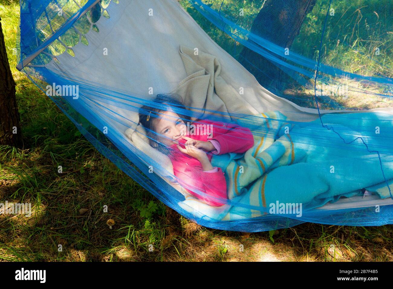 Kindermädchen erholt sich in einer sonnigen Hängematte mit Mückennetz im Wald. Stockfoto