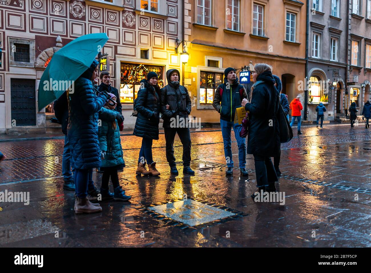 Warschau, Polen - 22. Dezember 2019: Gruppe von Touristen, die nachts mit Fremdenführer am Warszawa-Altstadtmarkt mit Regenschirm unterwegs sind Stockfoto