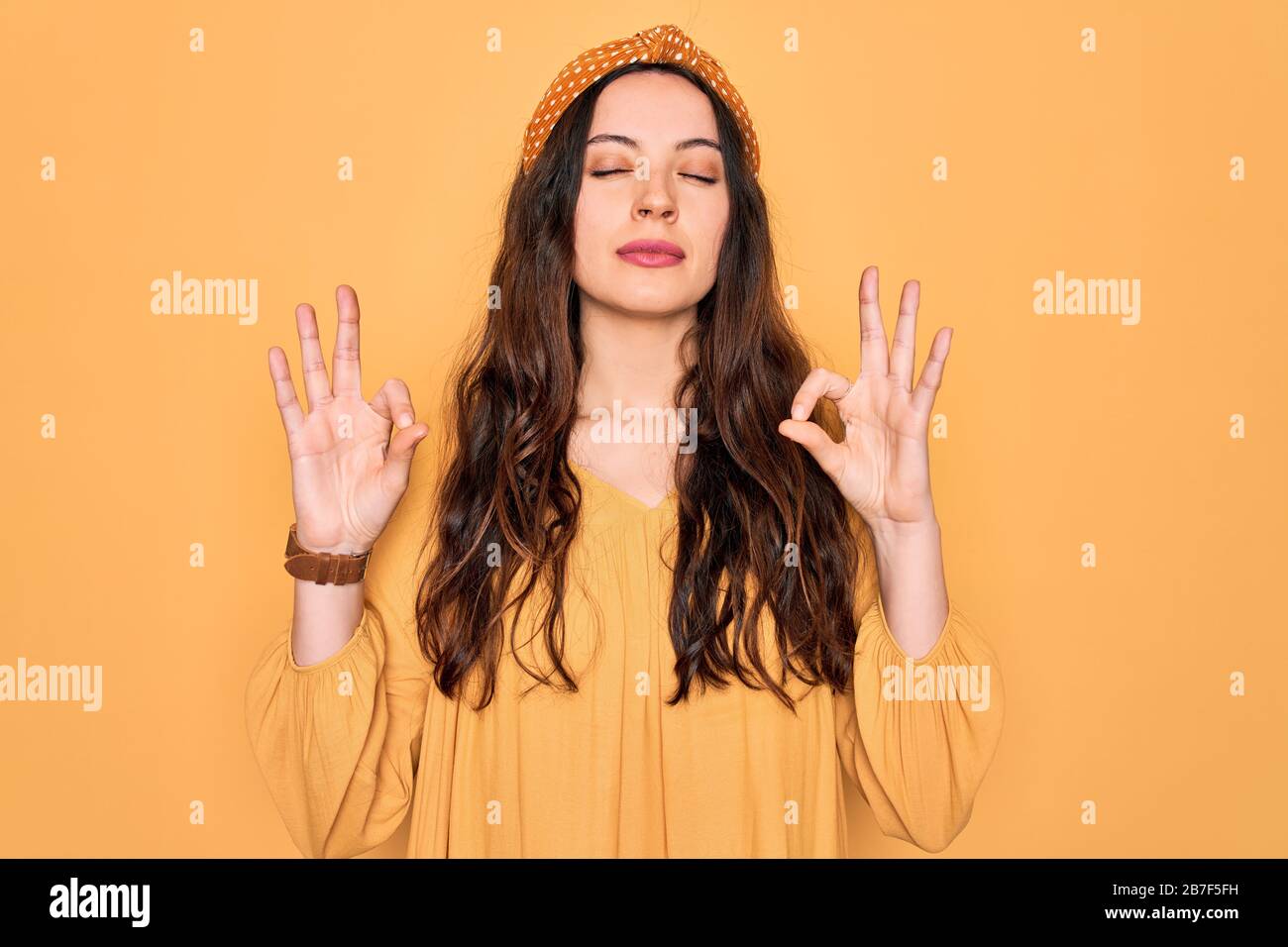 Junge schöne Frau mit legeren T-Shirts und diadem, die über gelbem Hintergrund stehen, entspannen Sie sich und lächeln Sie mit geschlossenen Augen, um die Meditationsgeste Wi zu tun Stockfoto