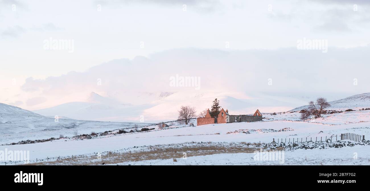 Der Blick auf einen schneebeschichteten Lochnagar am frühen Morgen leuchtet Sunshine den verlassenen Steading bei Blairglass im Cairngorms National Park auf Stockfoto