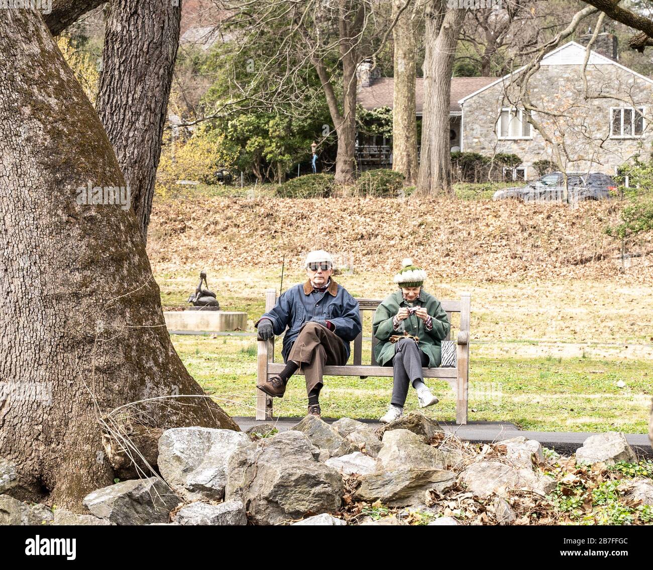 Berks County, Pennsylvania, USA - 14. März 2020: Ältere Paare, die das wärmere Wetter nutzen, sitzen gerne auf einer Bank im Park. Stockfoto