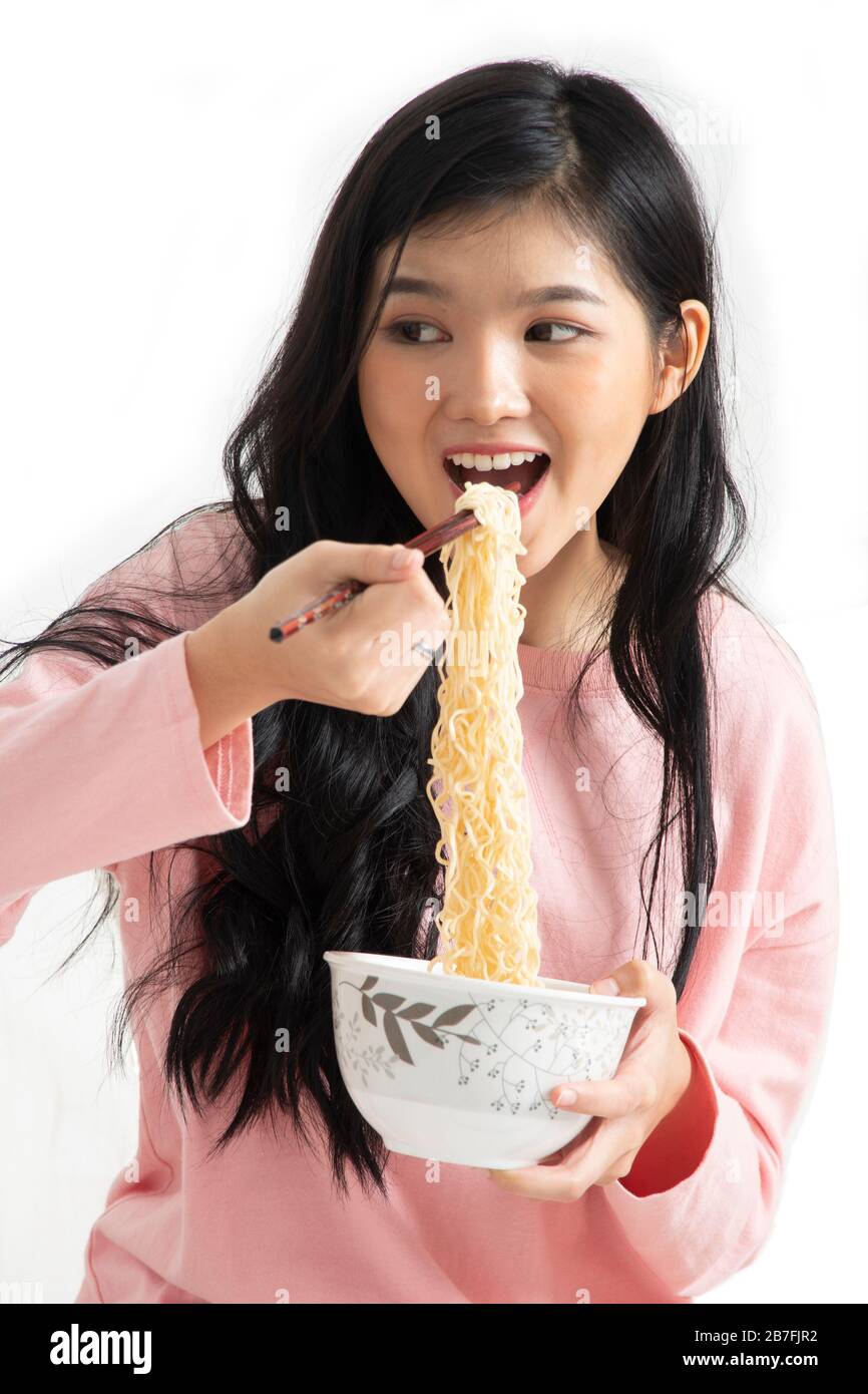 Mädchen essen gern, während sie mit Essstäbchen sofortige Nudeln in ihren Mund auf weißem Hintergrund halten. Stockfoto